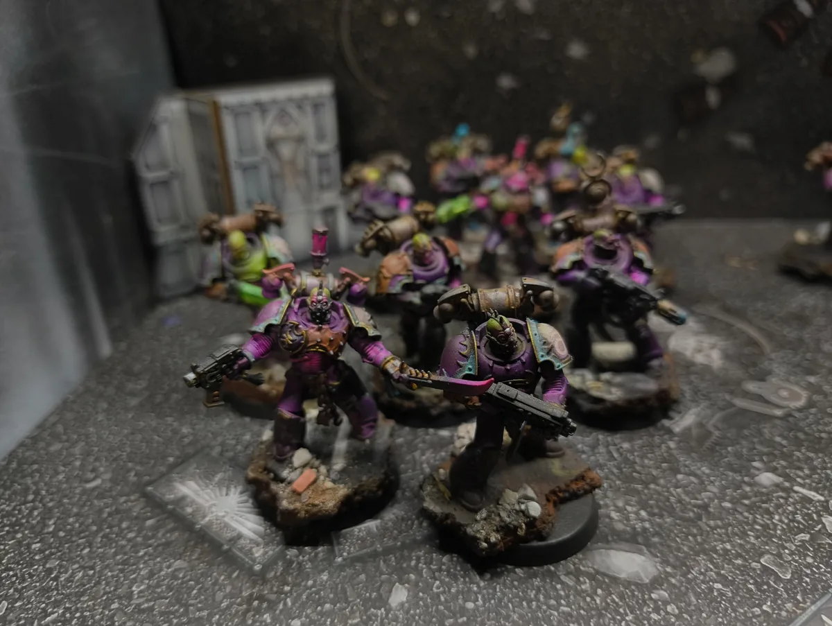Escuadra de Warhammer 40K con armaduras magenta sobre peanas de ruinas